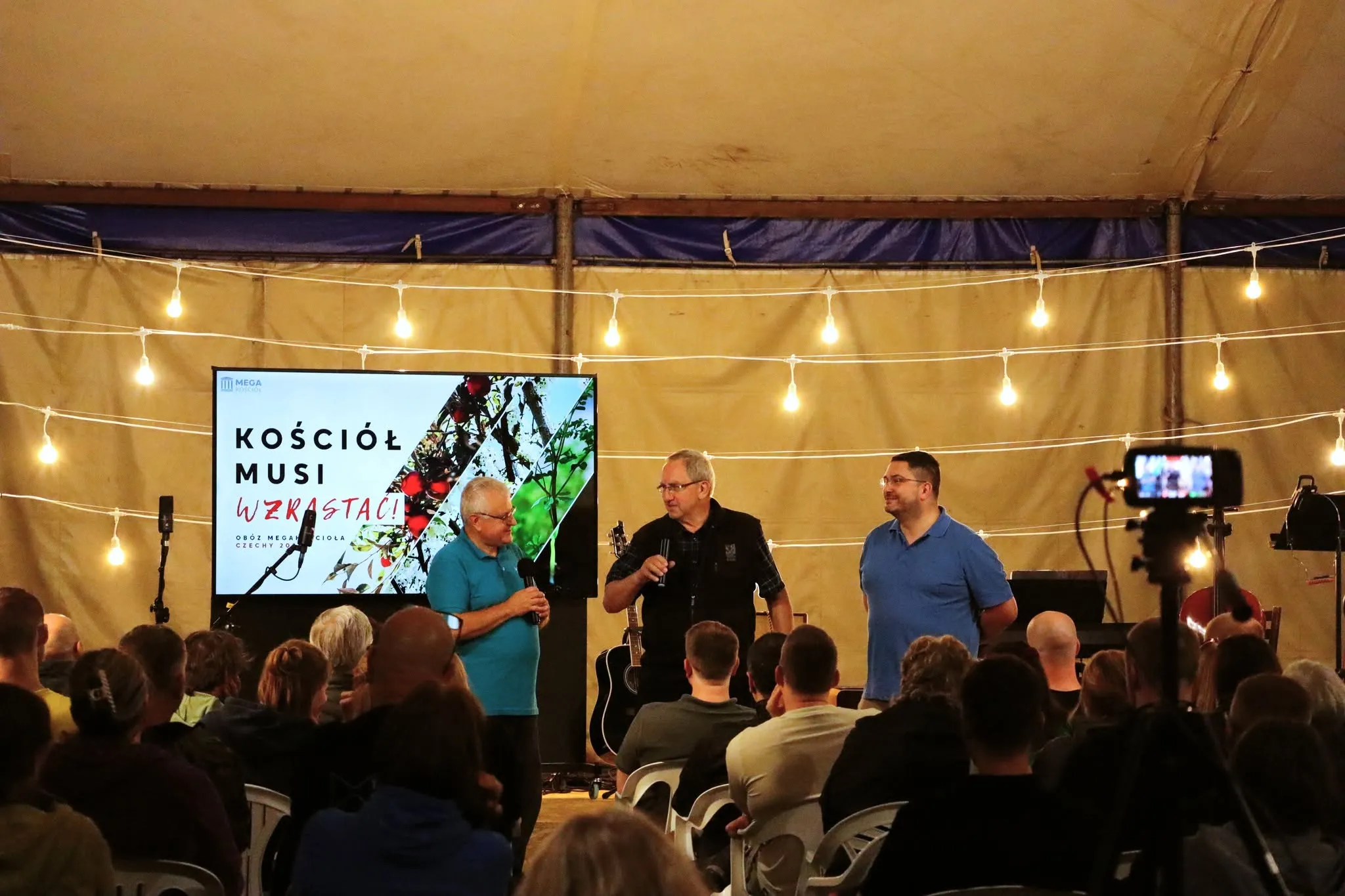 Three men on a camp tent stage; the screen reads that the church must grow.