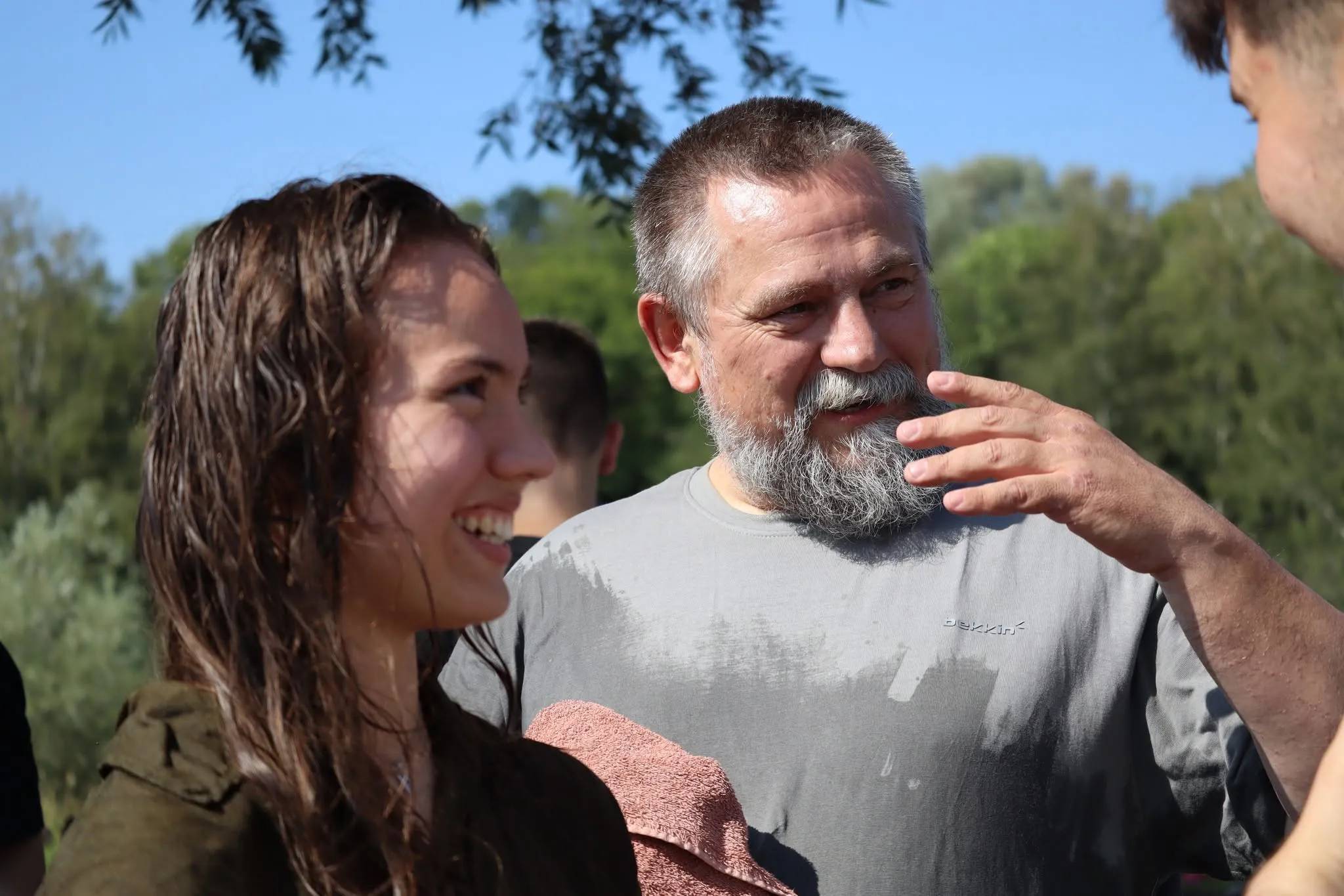 A smiling man with a grey beard talking with a young woman with wet hair.